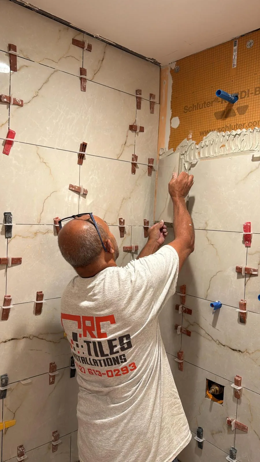 CRC installer setting white shower tile during a bathroom renovation